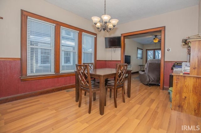 dining area featuring wood walls, ceiling fan with notable chandelier, a textured ceiling, and light hardwood / wood-style flooring