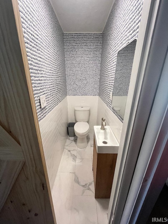 bathroom with toilet, sink, and tile walls