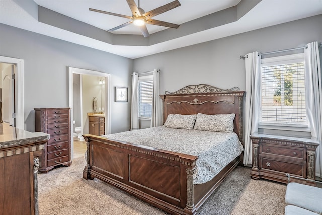 bedroom with ceiling fan, carpet, ensuite bathroom, a raised ceiling, and multiple windows