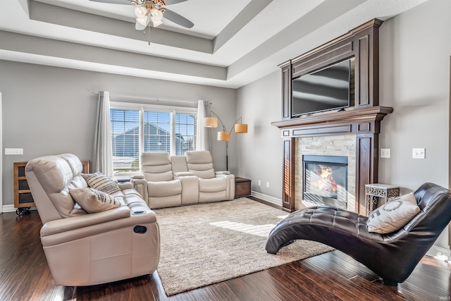 living room with a raised ceiling, ceiling fan, dark hardwood / wood-style floors, and a fireplace