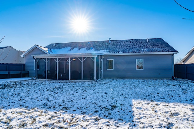 snow covered back of property featuring a sunroom