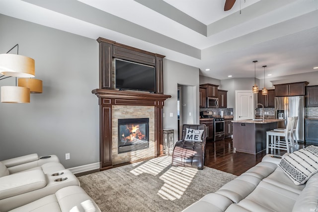 living room featuring a fireplace, ceiling fan, and dark wood-type flooring