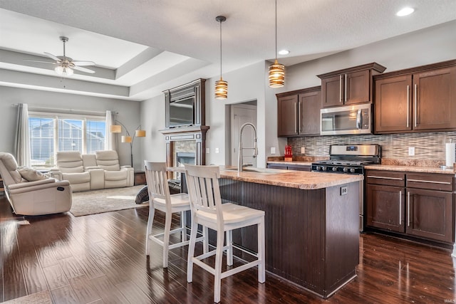 kitchen with stainless steel appliances, sink, backsplash, hanging light fixtures, and a center island with sink