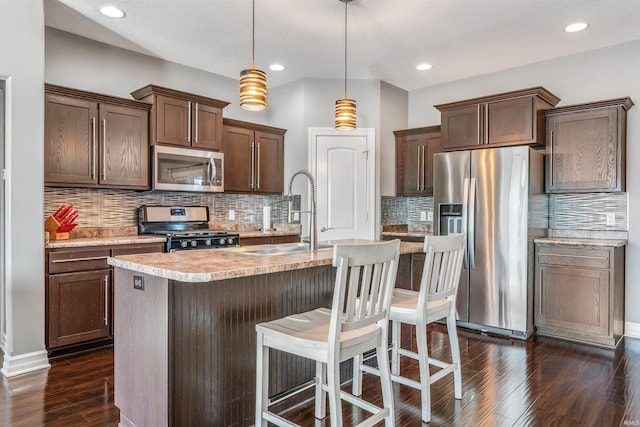 kitchen with sink, pendant lighting, appliances with stainless steel finishes, and an island with sink