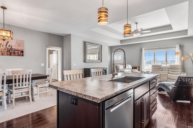 kitchen with dishwasher, a tray ceiling, a center island with sink, and dark brown cabinets