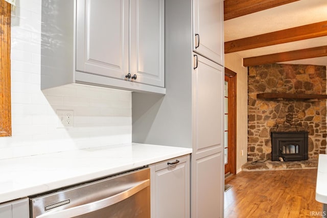 kitchen featuring light hardwood / wood-style floors, decorative backsplash, a wood stove, light stone countertops, and stainless steel dishwasher