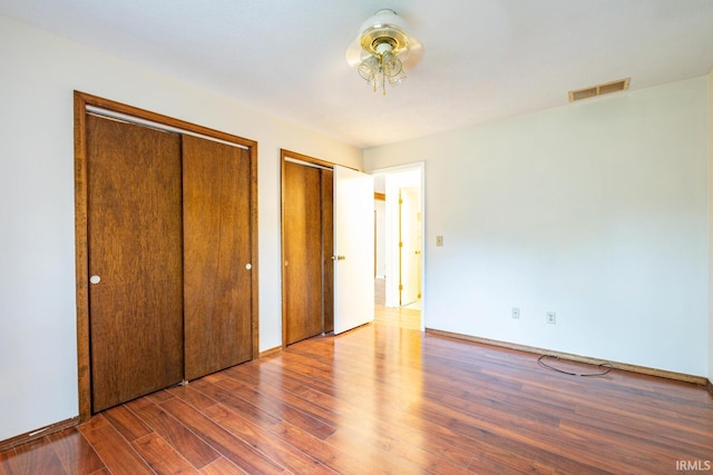 unfurnished bedroom featuring multiple closets and dark wood-type flooring