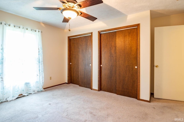 unfurnished bedroom with light carpet, ceiling fan, and two closets