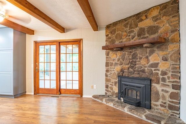 unfurnished living room featuring light wood-type flooring, a wood stove, and beamed ceiling