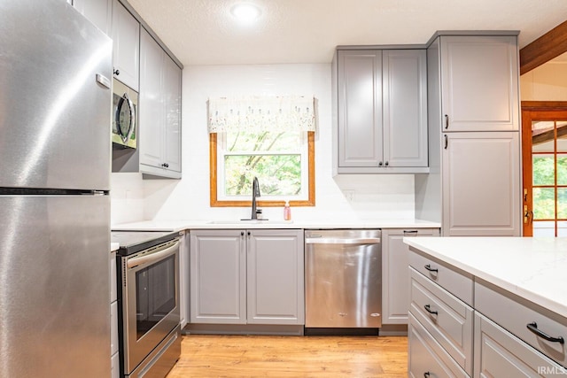 kitchen featuring gray cabinets, stainless steel appliances, light hardwood / wood-style flooring, light stone counters, and sink