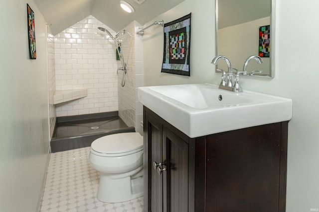 bathroom with a tile shower, vanity, lofted ceiling, and toilet