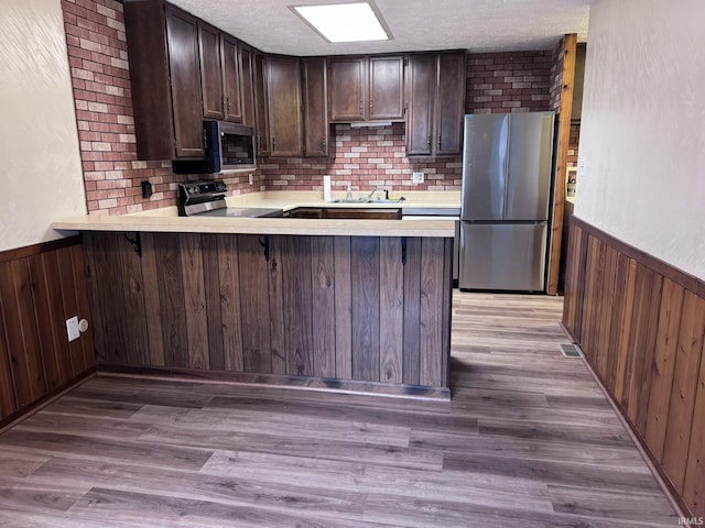 kitchen featuring a textured ceiling, dark brown cabinetry, stainless steel appliances, sink, and kitchen peninsula