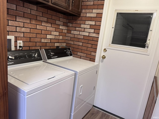 clothes washing area with cabinets, brick wall, dark hardwood / wood-style floors, and separate washer and dryer