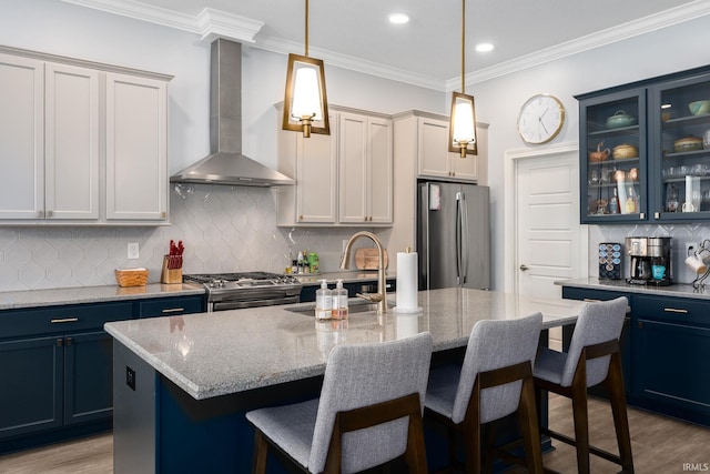 kitchen with light stone countertops, wall chimney range hood, stainless steel appliances, and a center island with sink