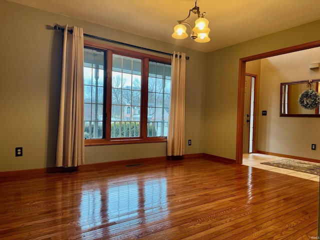 empty room with hardwood / wood-style floors and a notable chandelier