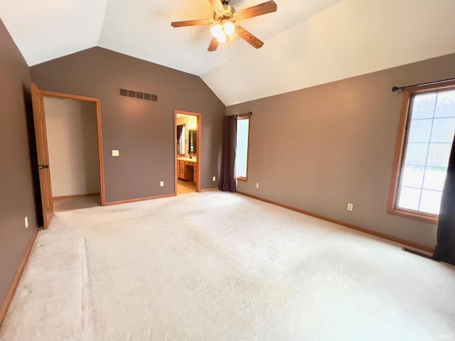 unfurnished bedroom with lofted ceiling, ensuite bath, multiple windows, light carpet, and ceiling fan