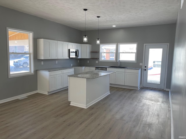 kitchen with decorative light fixtures, a center island, sink, white cabinetry, and appliances with stainless steel finishes