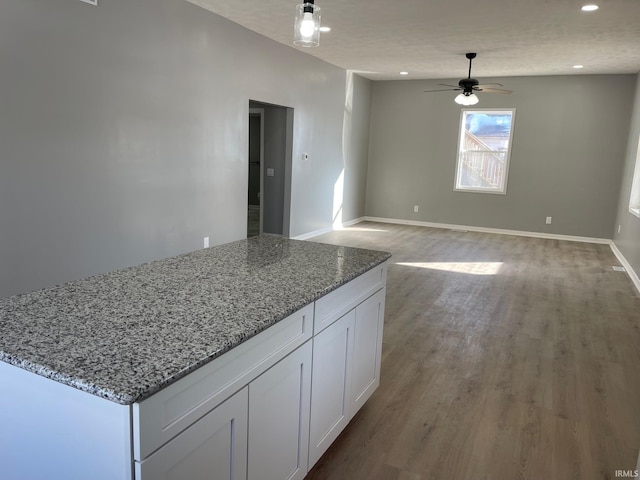 kitchen with ceiling fan, a center island, light wood-type flooring, light stone countertops, and white cabinets