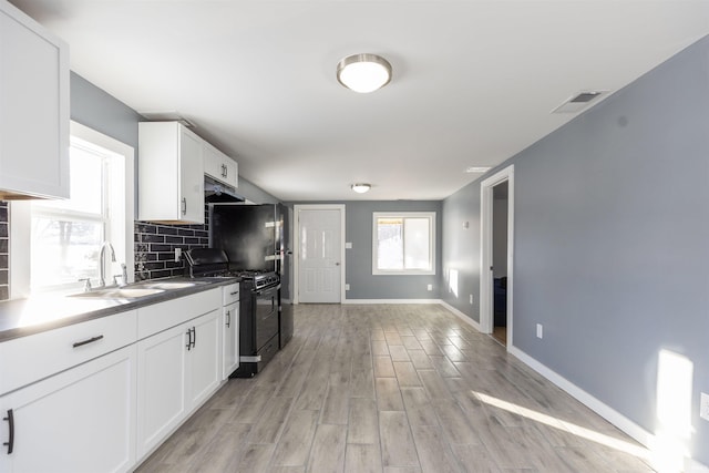 kitchen featuring tasteful backsplash, sink, light wood-type flooring, black gas range oven, and white cabinets