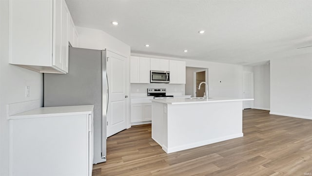 kitchen with appliances with stainless steel finishes, white cabinetry, an island with sink, sink, and light hardwood / wood-style flooring