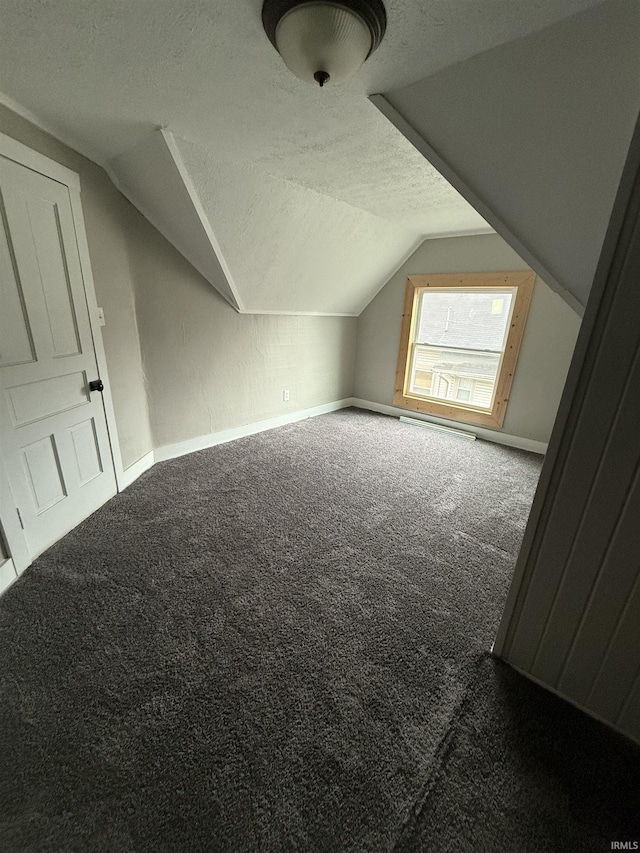 bonus room featuring a textured ceiling, vaulted ceiling, and dark colored carpet