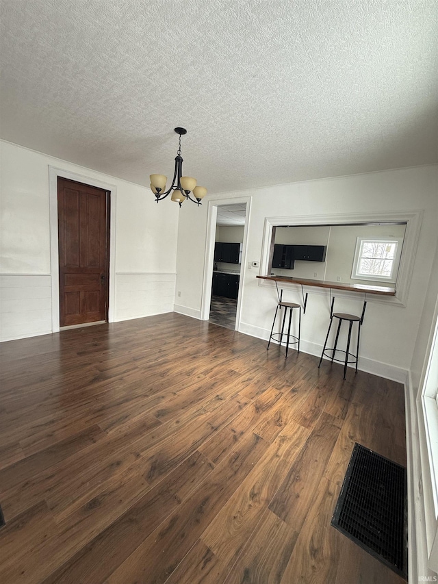 unfurnished living room featuring a textured ceiling, dark hardwood / wood-style floors, and an inviting chandelier