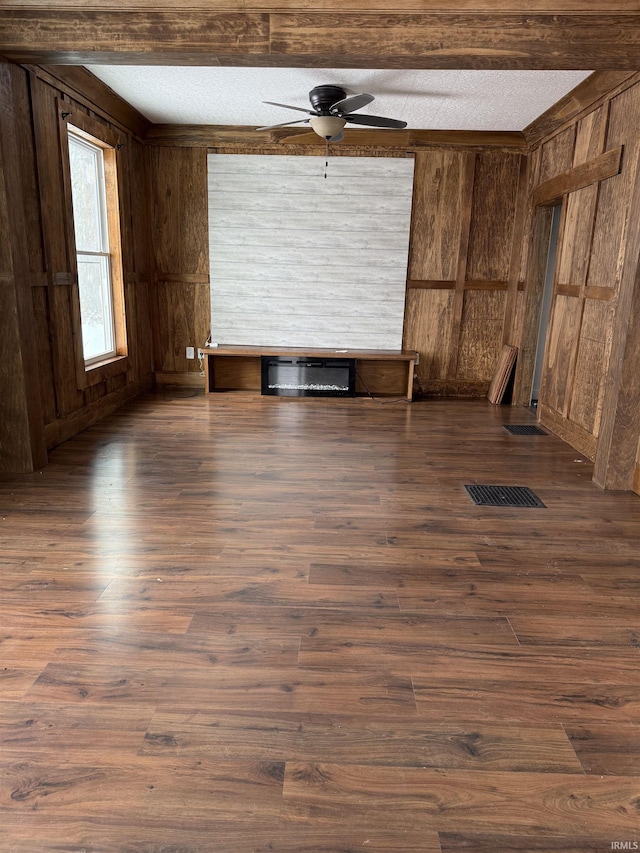 empty room with a textured ceiling, ceiling fan, dark hardwood / wood-style flooring, and wood walls