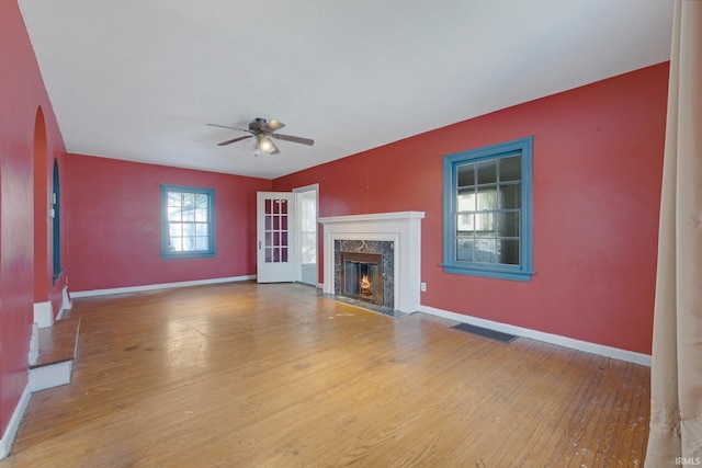 unfurnished living room with ceiling fan, a high end fireplace, and wood-type flooring