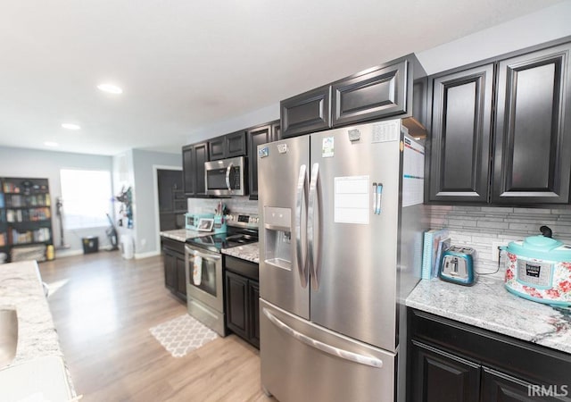 kitchen featuring tasteful backsplash, light stone countertops, stainless steel appliances, and light hardwood / wood-style flooring