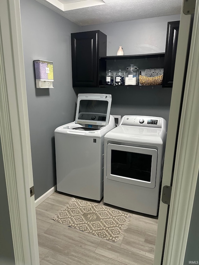 laundry area featuring washing machine and dryer, cabinets, a textured ceiling, and light wood-type flooring