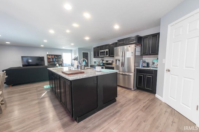 kitchen featuring a center island with sink, stainless steel appliances, backsplash, light stone countertops, and sink