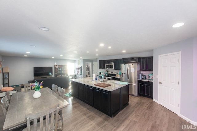 kitchen with light stone countertops, appliances with stainless steel finishes, an island with sink, light hardwood / wood-style floors, and decorative backsplash