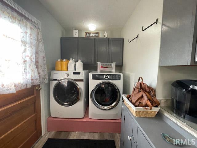 clothes washing area featuring wood-type flooring, washing machine and clothes dryer, and cabinets