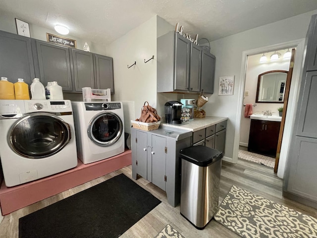 laundry area featuring a textured ceiling, cabinets, washer and dryer, and light hardwood / wood-style flooring