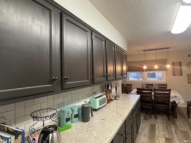 kitchen featuring a textured ceiling, hardwood / wood-style flooring, pendant lighting, and backsplash