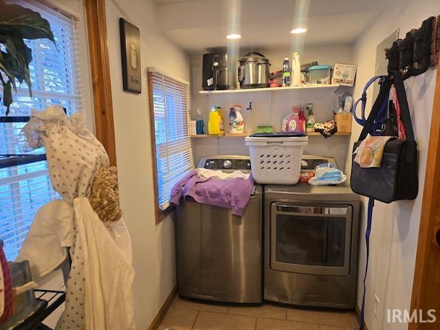 clothes washing area with washing machine and dryer, a wealth of natural light, and light tile patterned floors