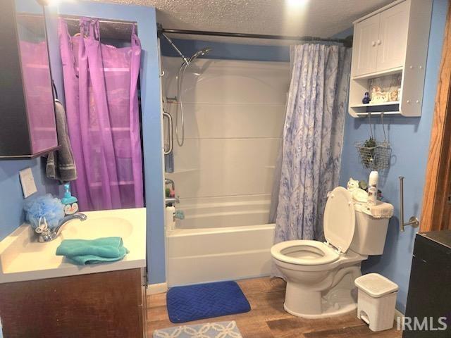 full bathroom with shower / tub combo with curtain, hardwood / wood-style flooring, vanity, toilet, and a textured ceiling