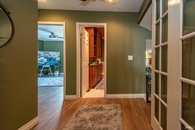 corridor featuring a textured ceiling, french doors, and light wood-type flooring