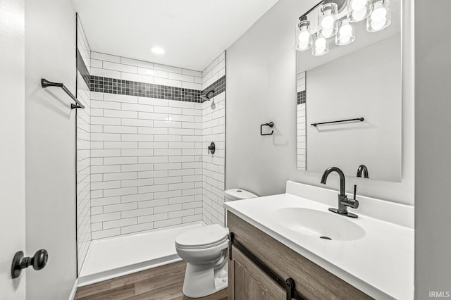 bathroom with toilet, vanity, a tile shower, and hardwood / wood-style flooring