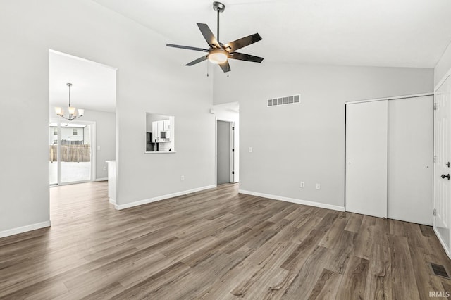 unfurnished living room with high vaulted ceiling, ceiling fan with notable chandelier, and hardwood / wood-style floors