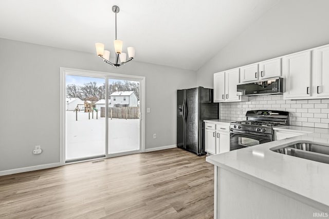 kitchen with white cabinets, black appliances, lofted ceiling, hanging light fixtures, and a notable chandelier