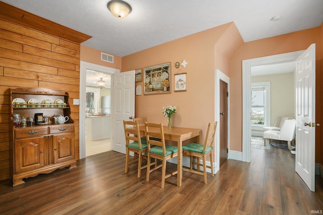 dining area with dark wood-type flooring, a textured ceiling, and wood walls