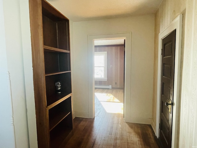 corridor with a baseboard heating unit and dark hardwood / wood-style flooring