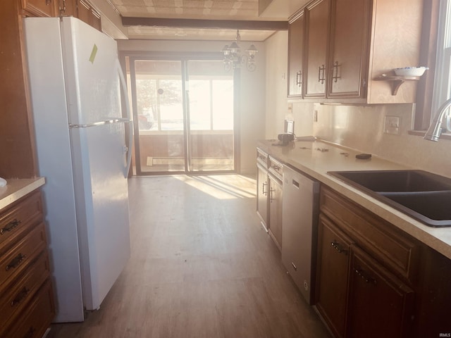 kitchen with sink, hanging light fixtures, dishwashing machine, white refrigerator, and a chandelier