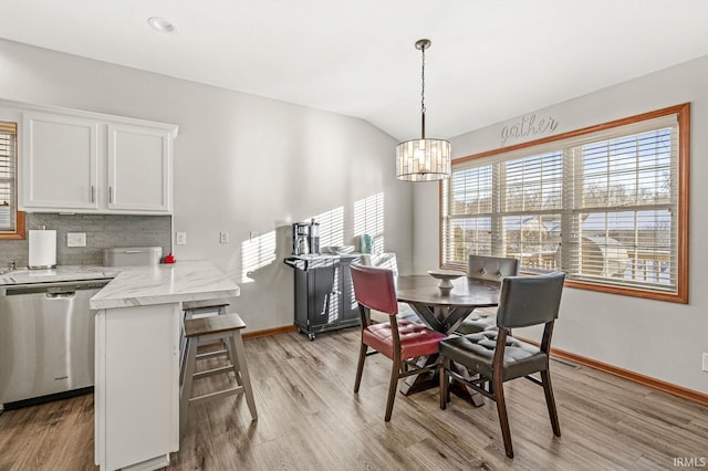 dining space with an inviting chandelier, lofted ceiling, and light hardwood / wood-style flooring