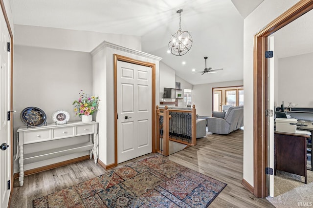 foyer featuring ceiling fan with notable chandelier, light hardwood / wood-style flooring, and vaulted ceiling