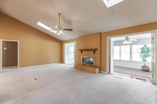 unfurnished living room with a brick fireplace, a wealth of natural light, vaulted ceiling with skylight, and ceiling fan