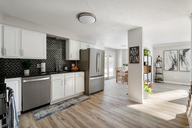 kitchen with white cabinets, appliances with stainless steel finishes, sink, backsplash, and light wood-type flooring