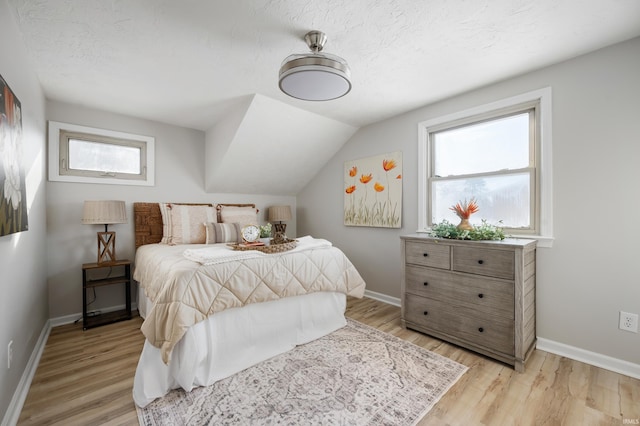 bedroom featuring a textured ceiling, light hardwood / wood-style flooring, and vaulted ceiling