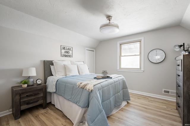 bedroom with a textured ceiling, lofted ceiling, and light wood-type flooring